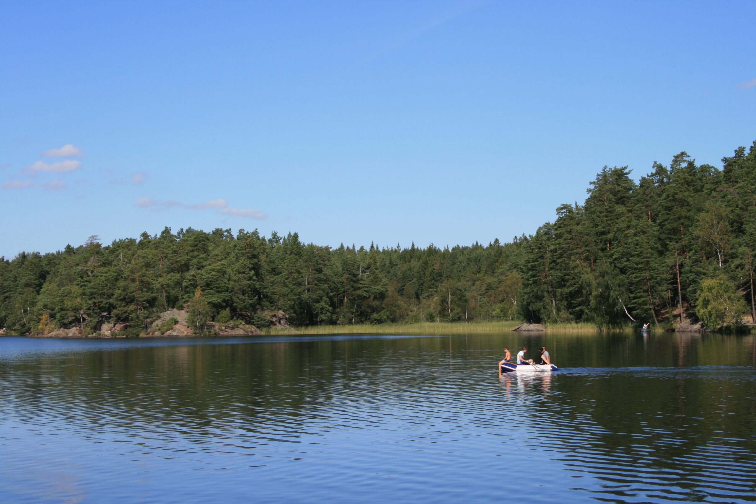 Sjö med tre som badare och skog i bakgrunden